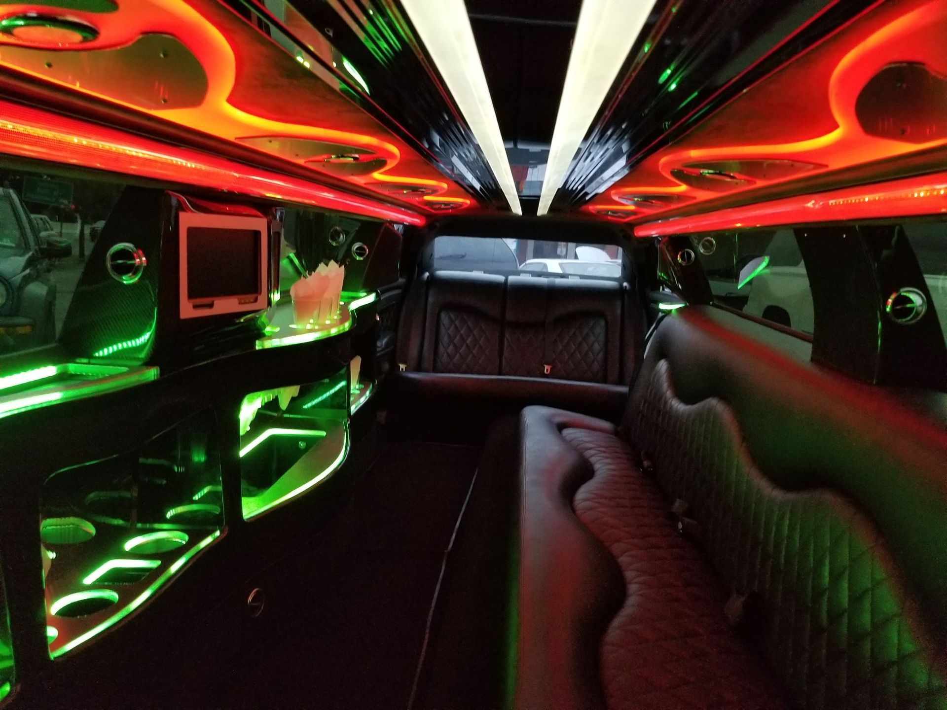 Inside of a limousine with neon green and red lights, black interior, and a TV screen.