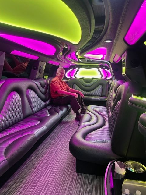 Man sits in a luxurious limo with purple and green interior lights.
