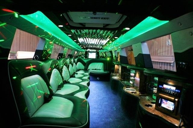 Inside of a limousine, green and black interior with neon green lights and disco ball.
