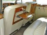 Interior of a classic car, beige leather seats and a wooden fold-down table.