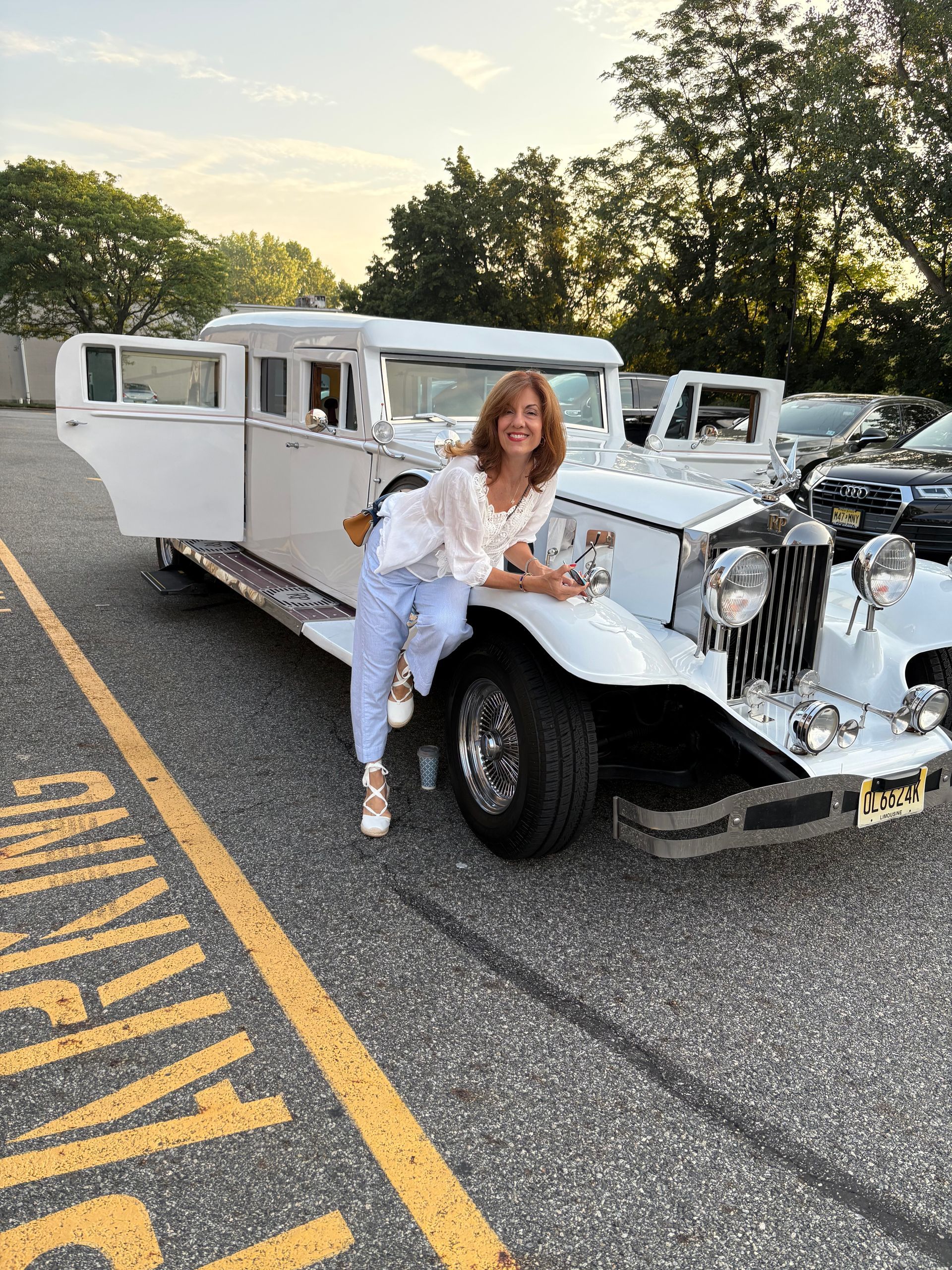 Woman poses next to a white vintage limousine in parking lot.
