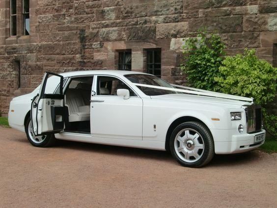 White Rolls-Royce Phantom with open doors, parked in front of a stone building.