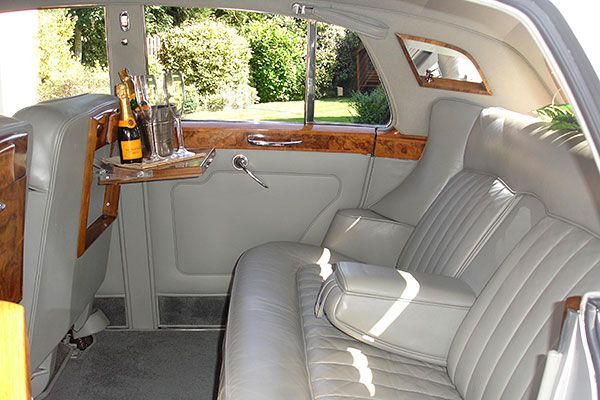Interior of a Rolls Royce. Cream leather seats, wooden trim, champagne bottle and glasses on a tray.