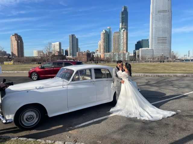 Bride and groom beside a white vintage car, with a city skyline in the background.