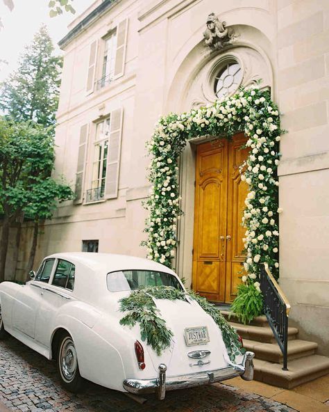White vintage car parked in front of a building with floral arch over a wooden door.
