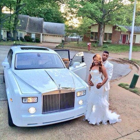 Couple in formal wear posing beside a white Rolls Royce in front of a house.