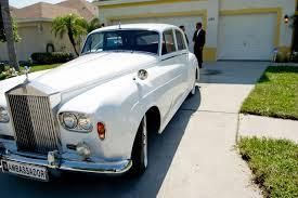 White Rolls-Royce parked in front of a house, with a man in a suit standing nearby.