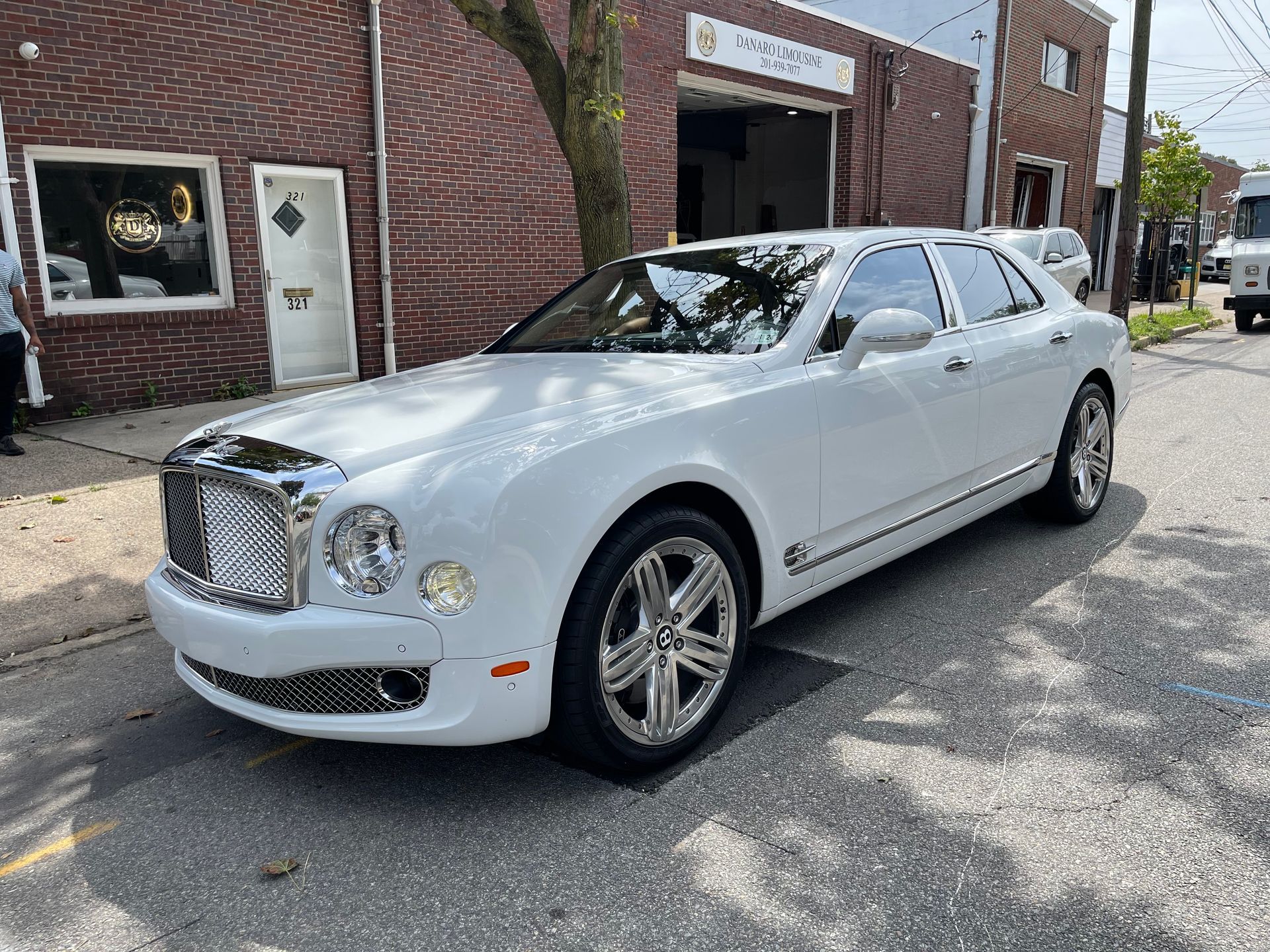 White Bentley Mulsanne parked on a city street in front of a brick building with a business sign.
