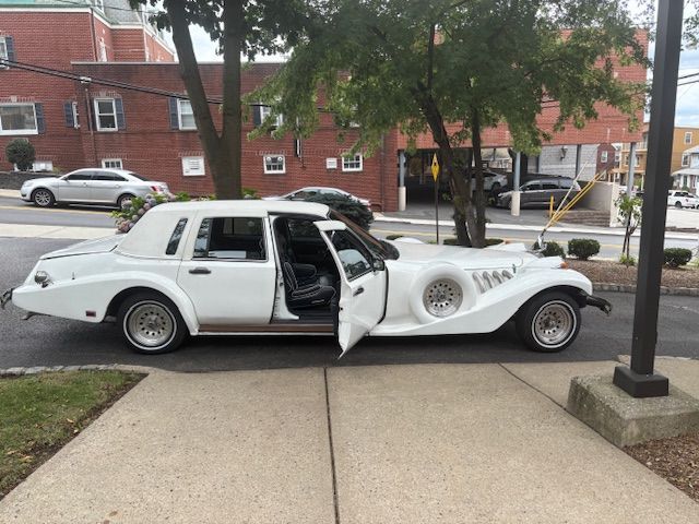 White custom-built car with open doors parked on a sidewalk.