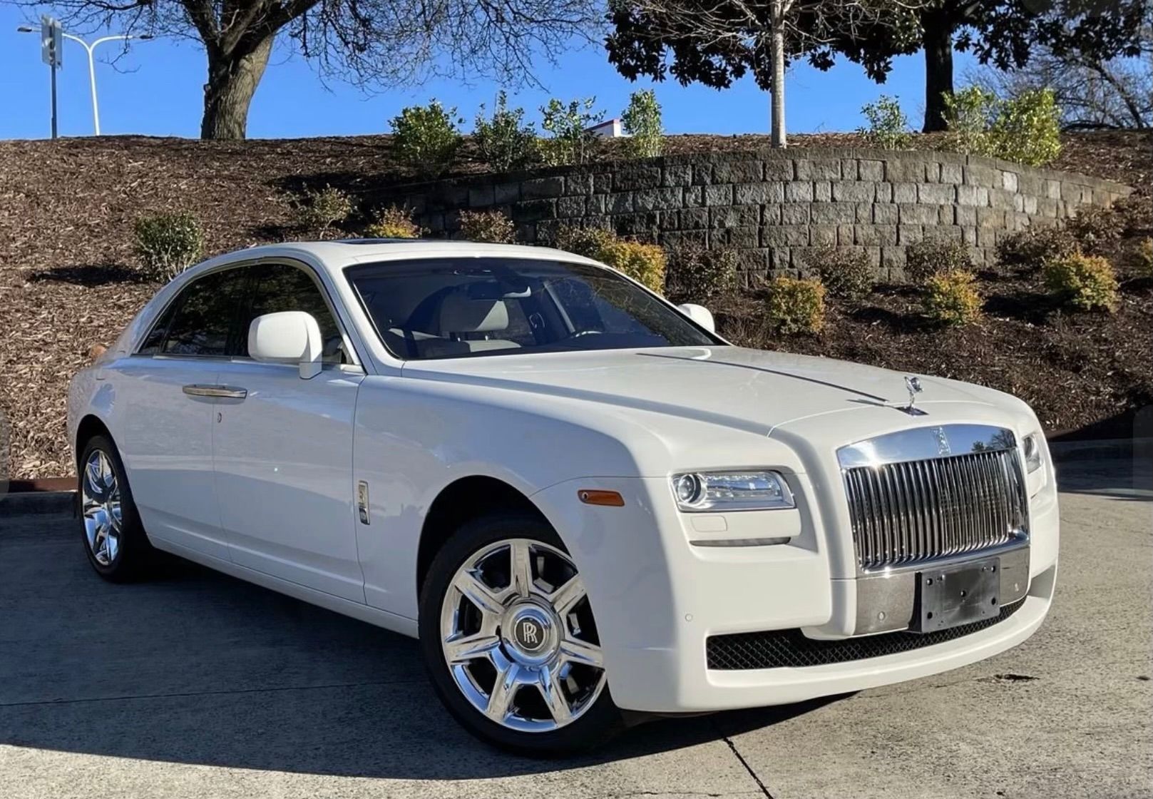 White Rolls Royce coupe parked on a sunny day, in front of a stone wall.
