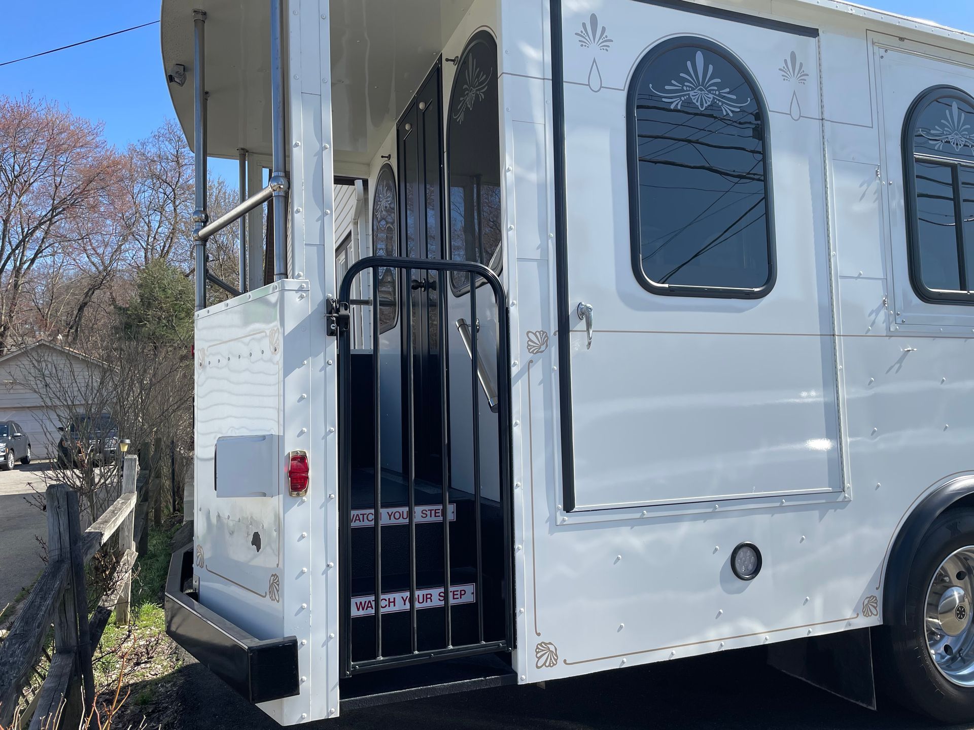 White trolley with open entrance, black gate, and steps, parked outdoors.