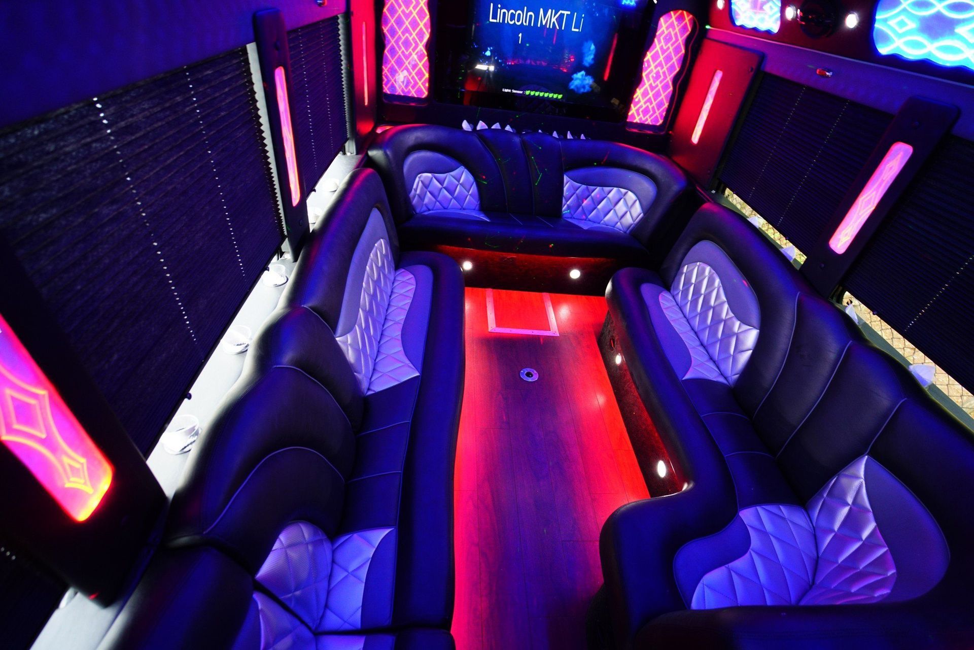 Interior of a party bus with black leather seating, neon lights, and mirrored walls.