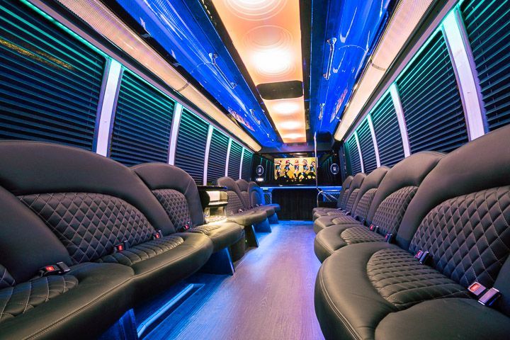 Interior of a black party bus with diamond-stitched seats, neon lights, and a bar area.