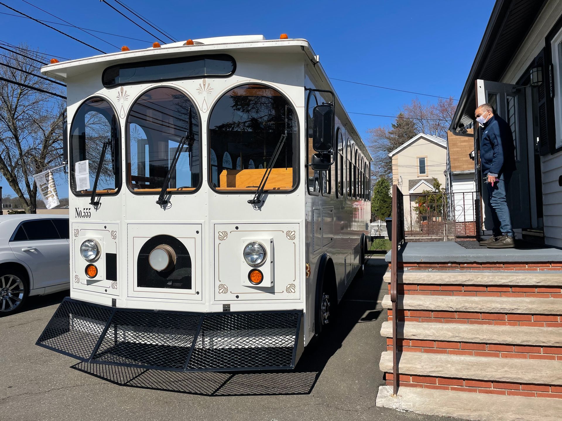 White trolley parked near a building; a man with a mask stands in the doorway.