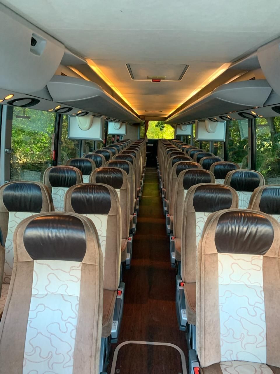 Interior of a bus with rows of tan and brown seats, wooden floor, and overhead lighting.