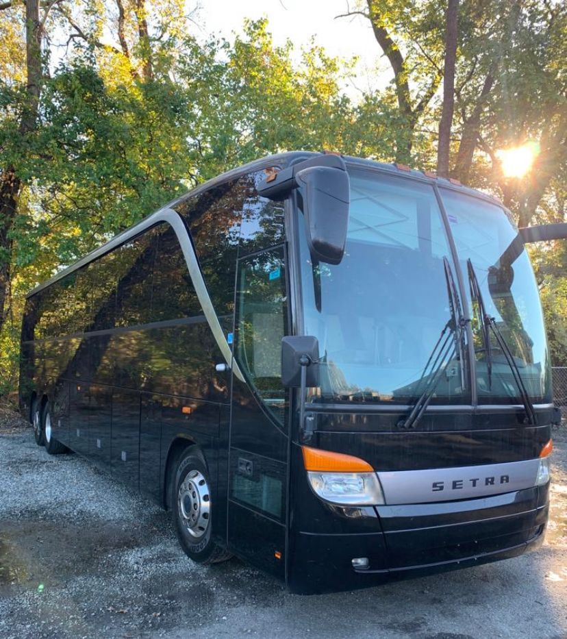 Black Setra coach bus parked on gravel. Bright sunlight in the background.