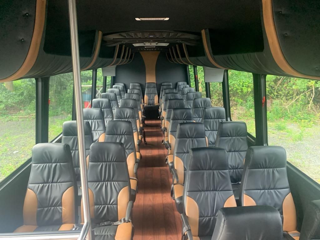 Interior of a coach bus, with rows of black and tan seats and a wooden floor.