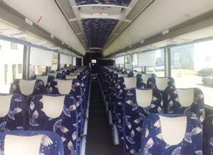 Interior of a bus with blue patterned seats, long rows, overhead storage, and windows.