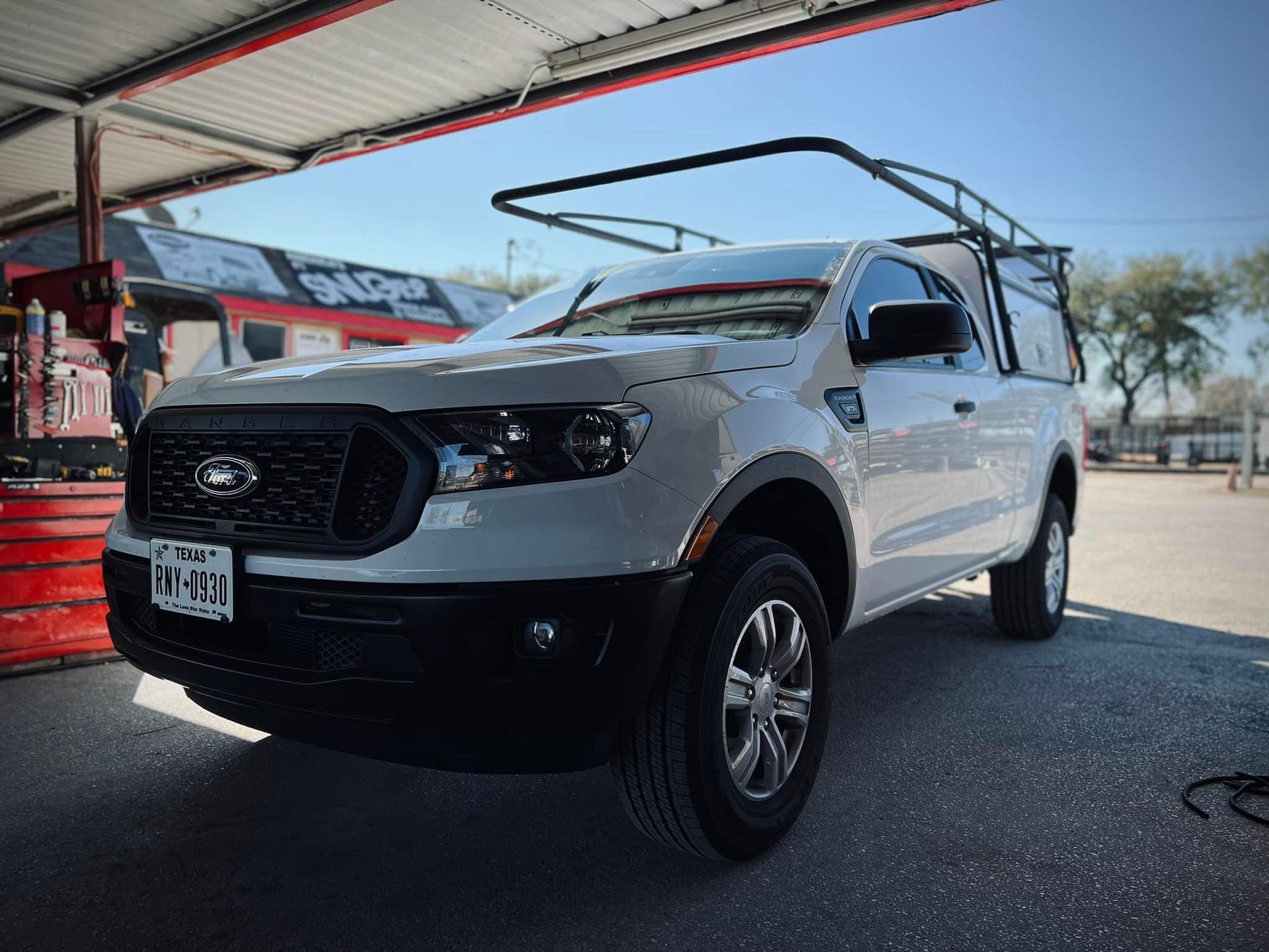 White Ford Ranger pickup truck with black trim, parked under a carport, with a black rack on top.