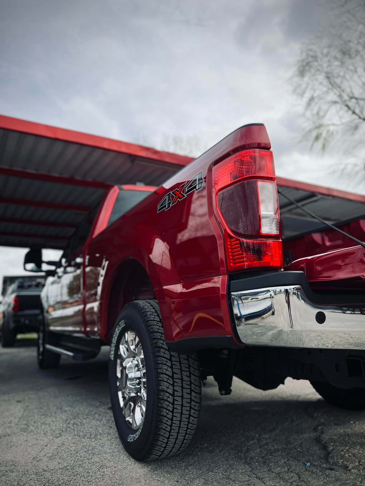 Red pickup truck parked under a red awning, chrome wheels, and taillight visible.