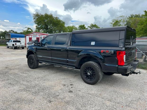 Black Ford pickup truck with a black camper shell parked on gravel.