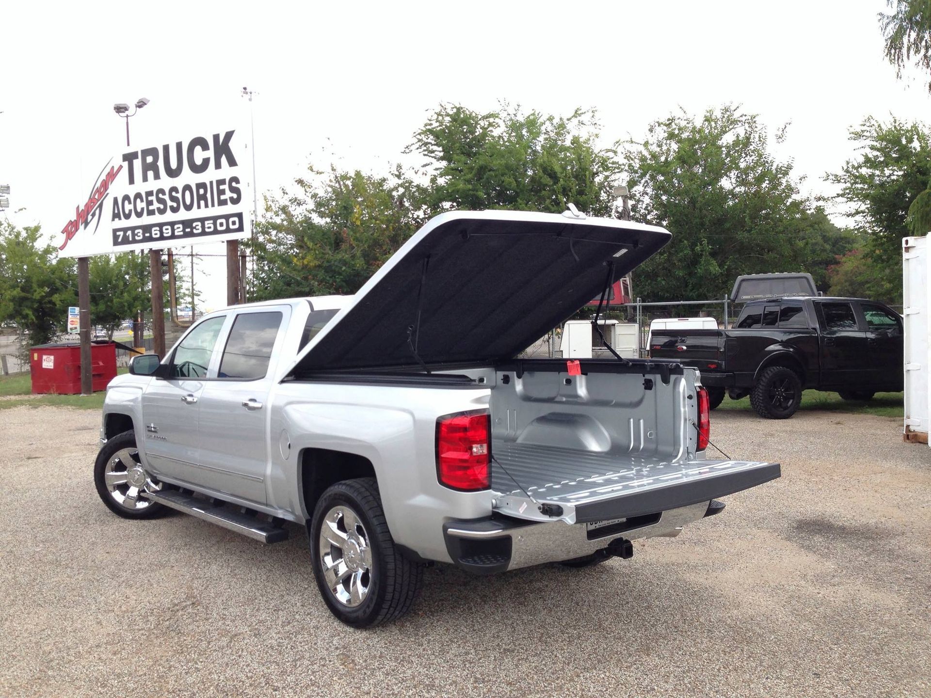 Silver pickup truck with open bed cover, parked at a truck accessories store, tailgate down.