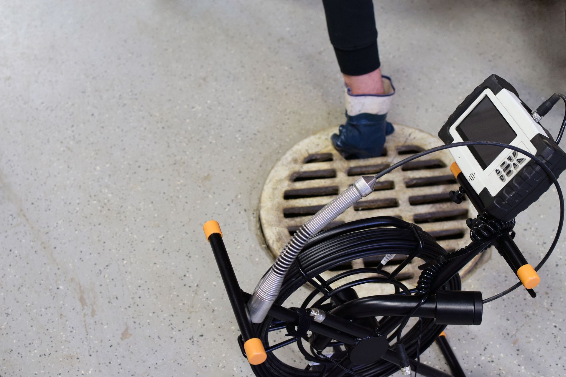 Person standing on a round drain grate beside a black wheelchair with orange-tipped handles