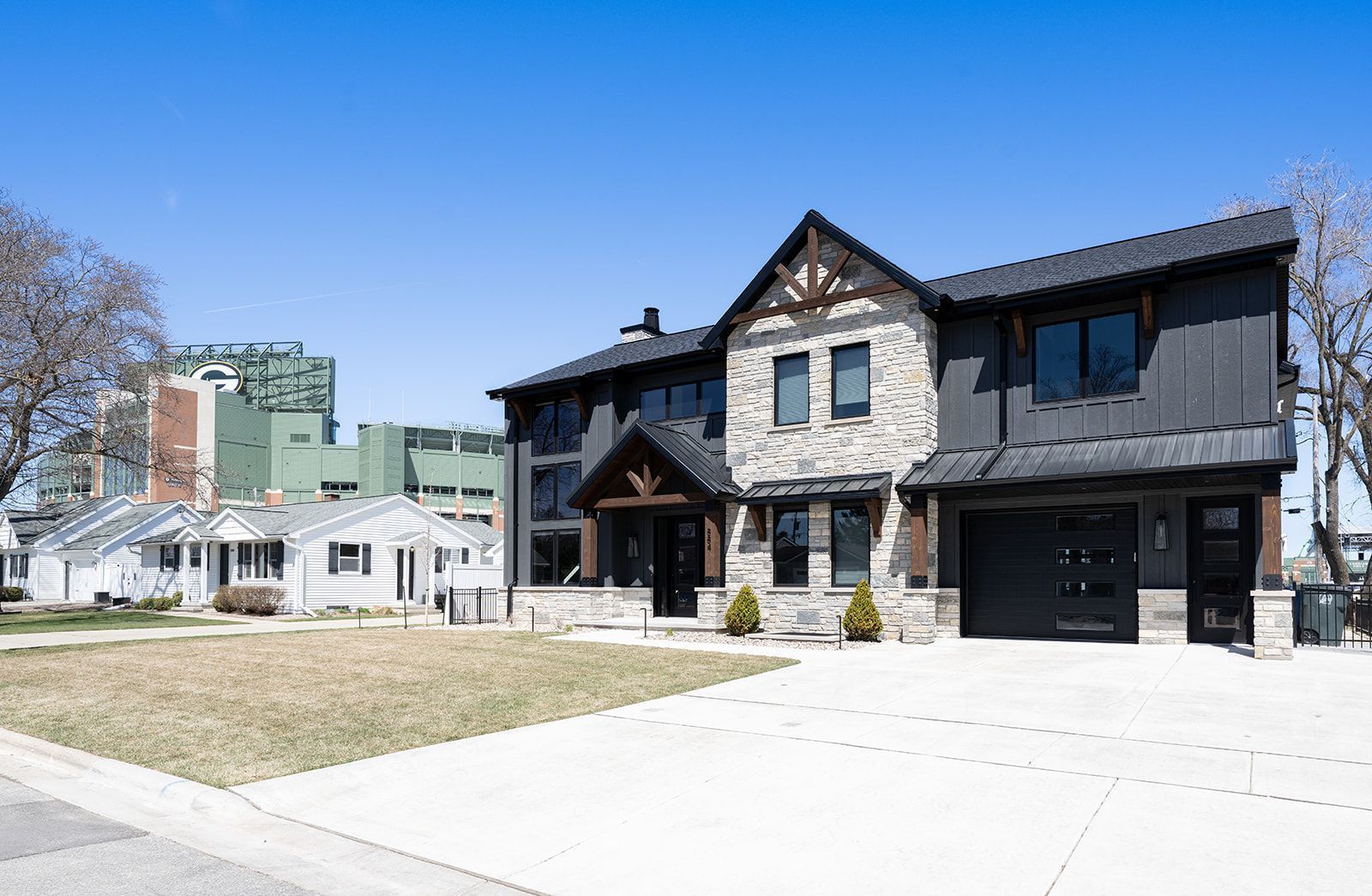 Modern two-story house with stone and black siding, garage, and lawn; sunny day.