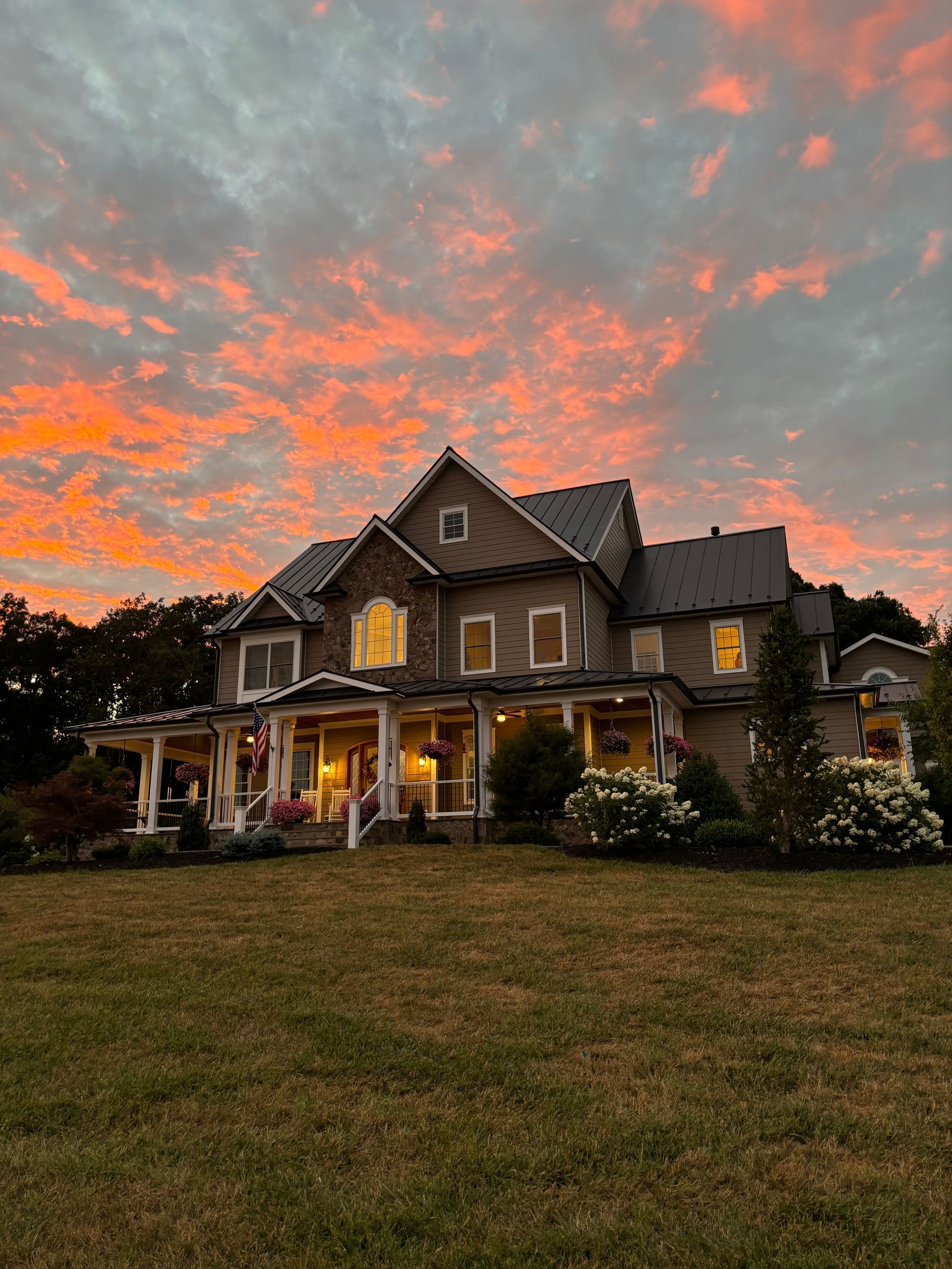 A large house with a porch and a sunset in the background.