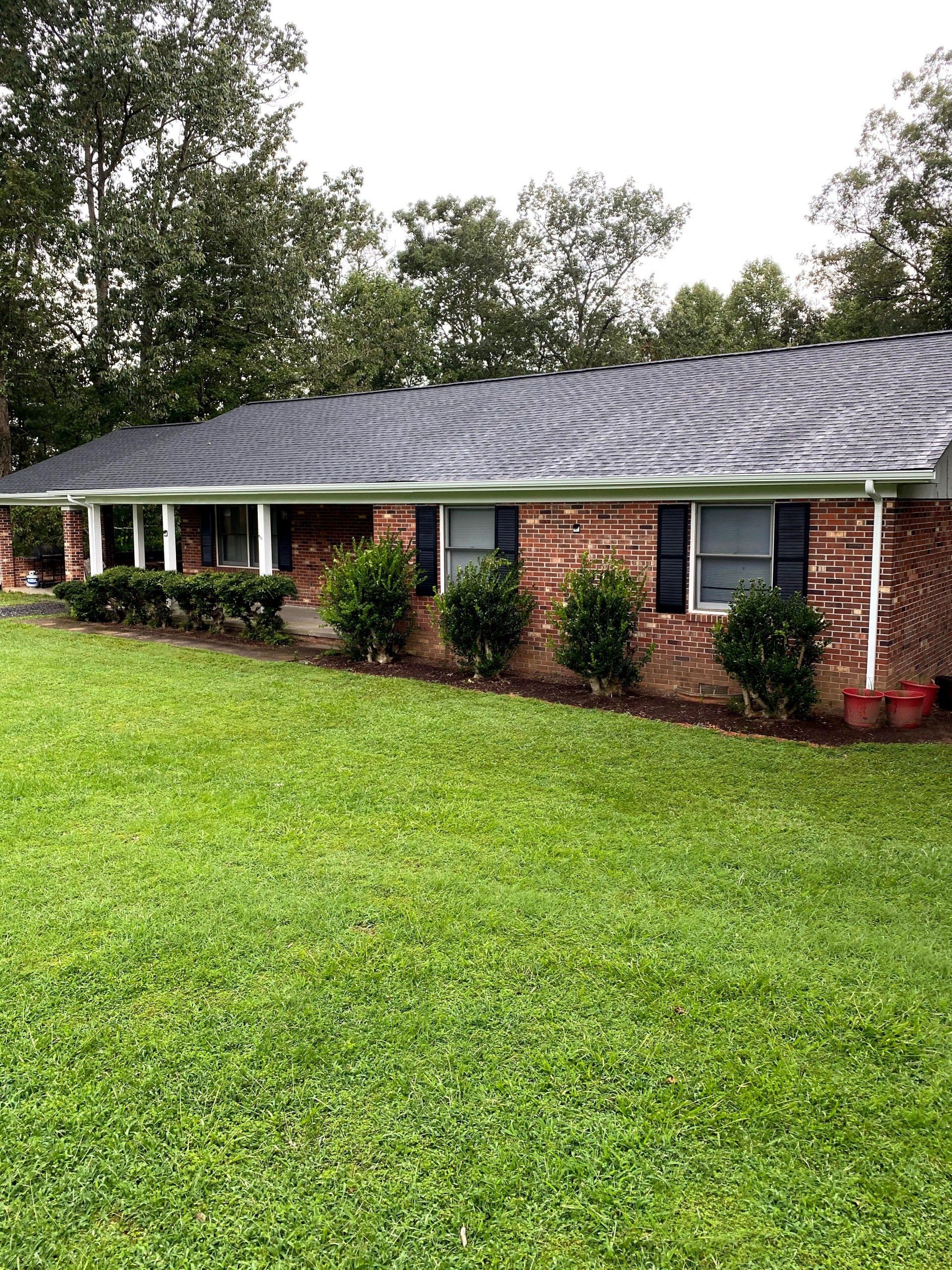 A brick house with a gray roof and a large lawn in front of it.
