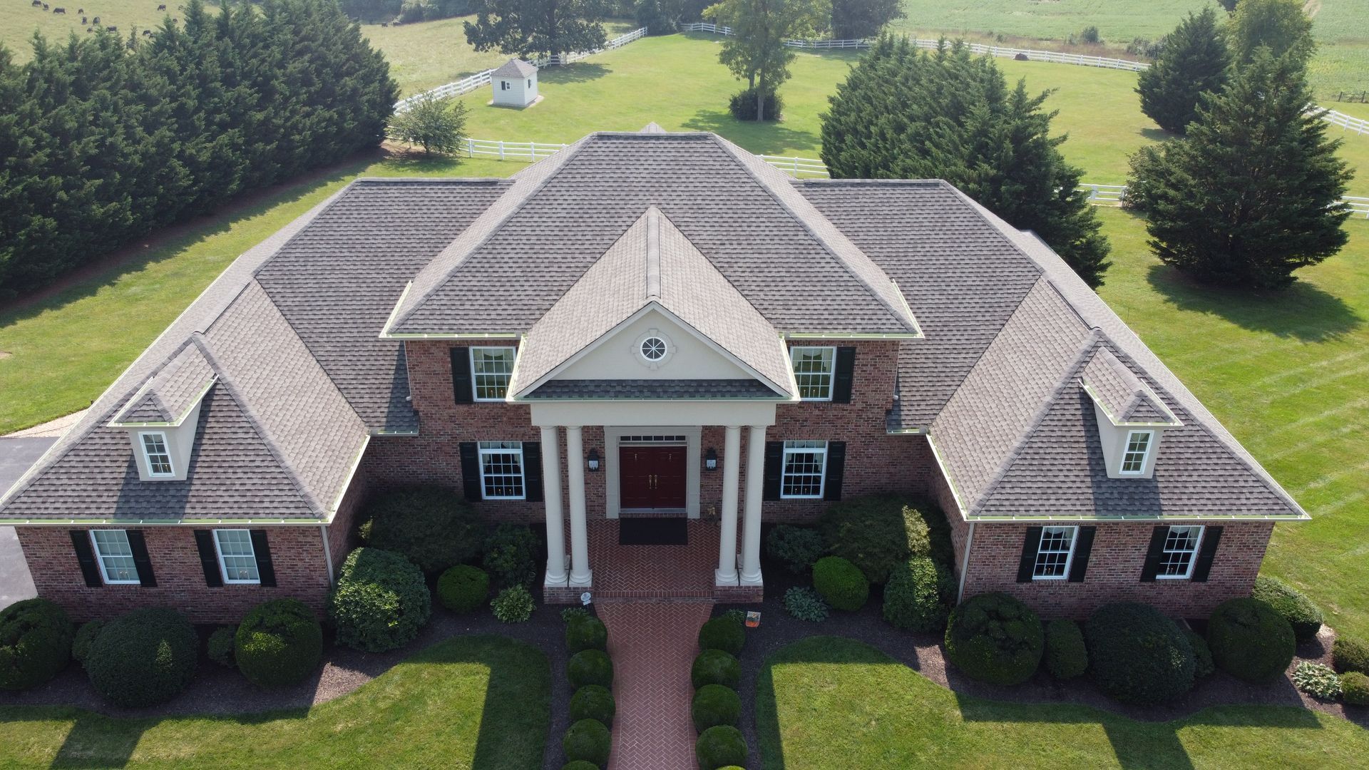 An aerial view of a large brick house with a gray roof