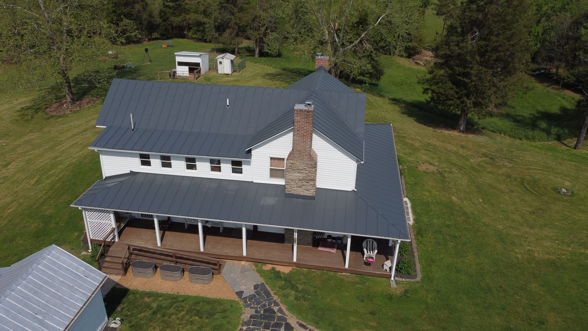 An aerial view of a large white house with a metal roof surrounded by trees.