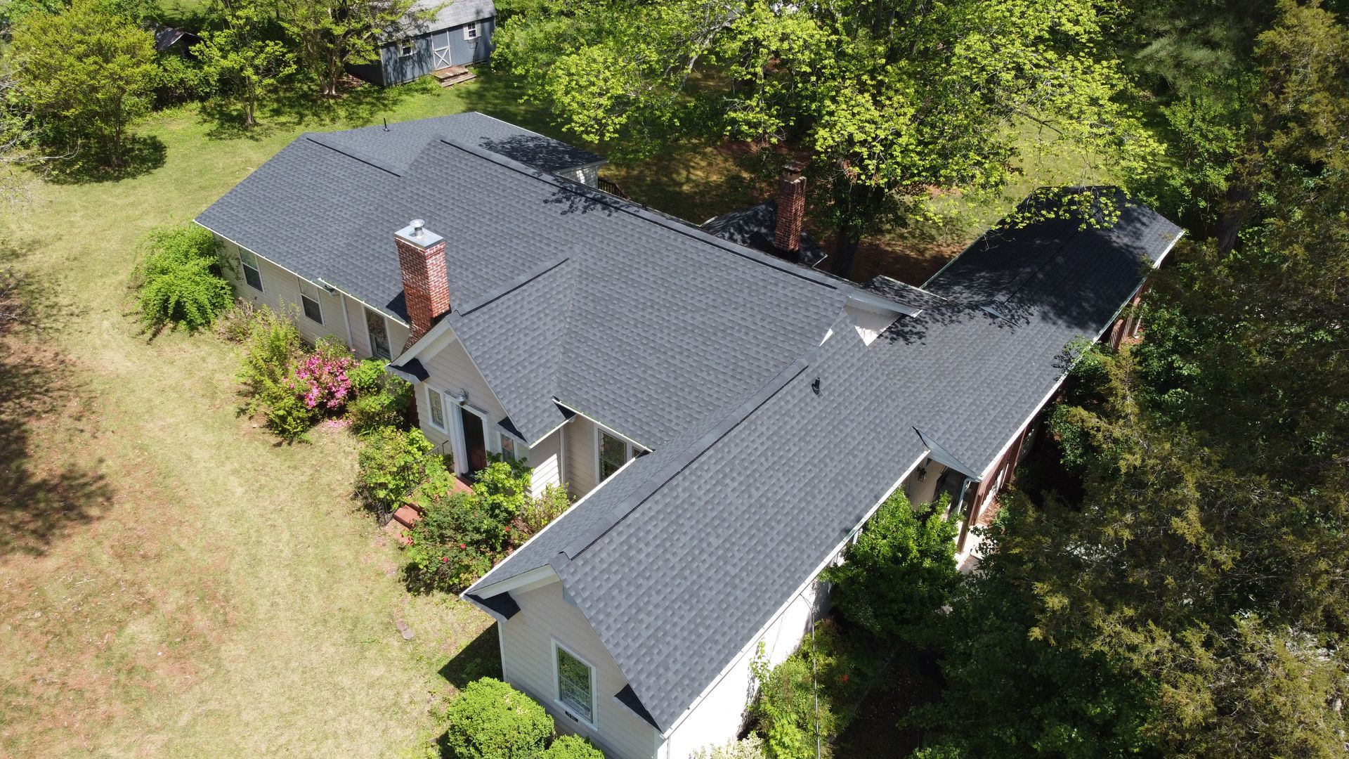 An aerial view of a large white house with a black roof surrounded by trees.