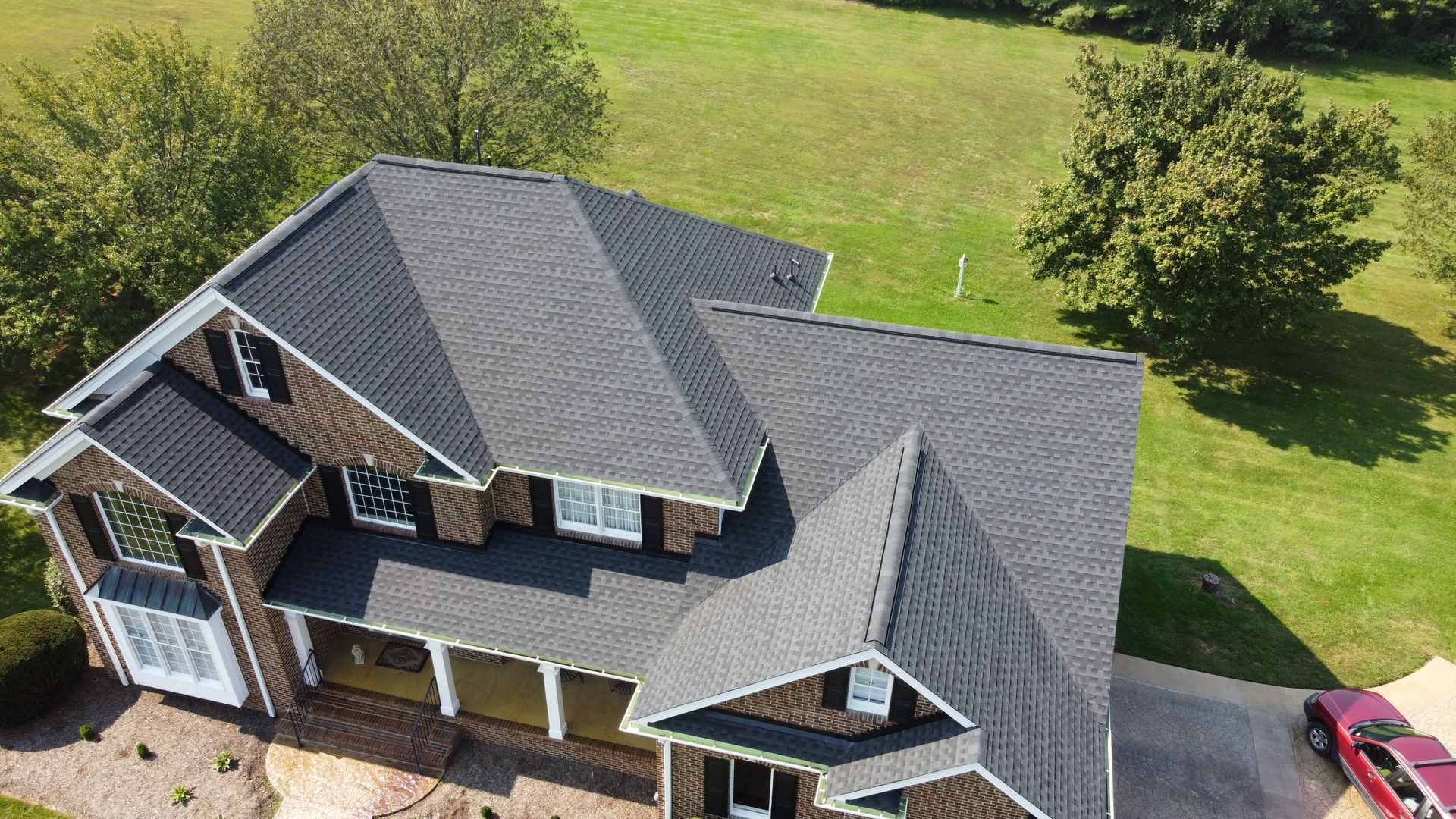 An aerial view of a large house with a gray roof and a red car parked in front of it.