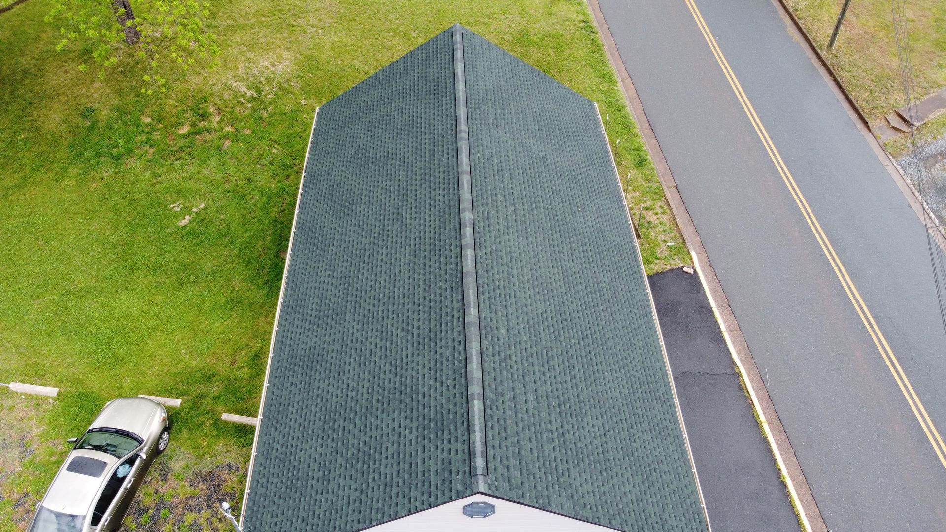 An aerial view of a house with a green roof and a car parked in front of it.