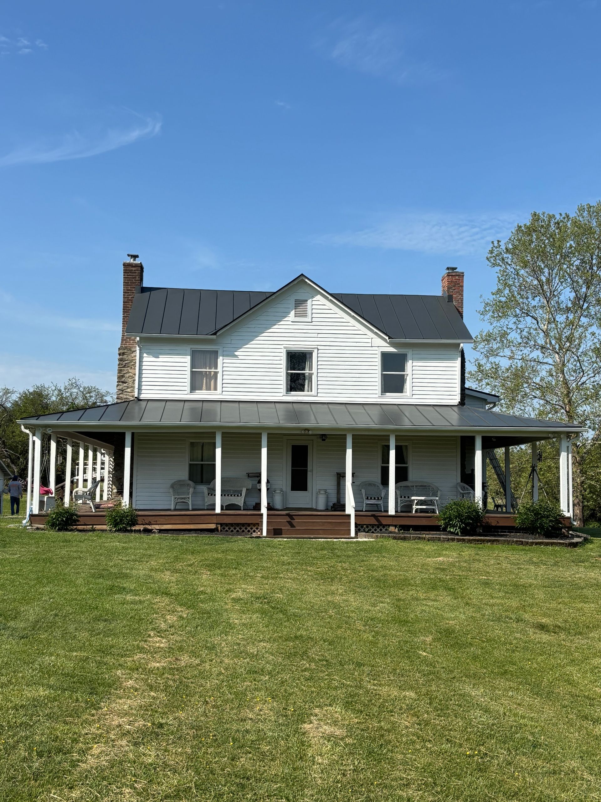 A large white house with a porch is sitting on top of a lush green field.
