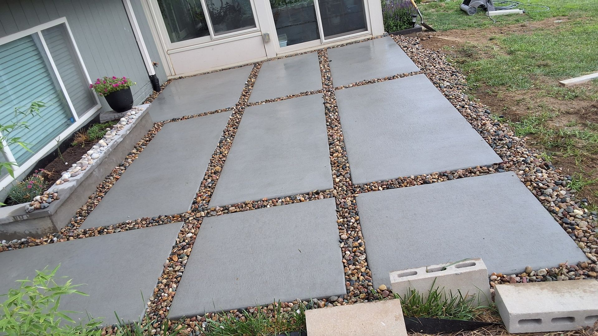A modern concrete patio featuring large rectangular slabs separated by rows of decorative gravel next to a house exterior.