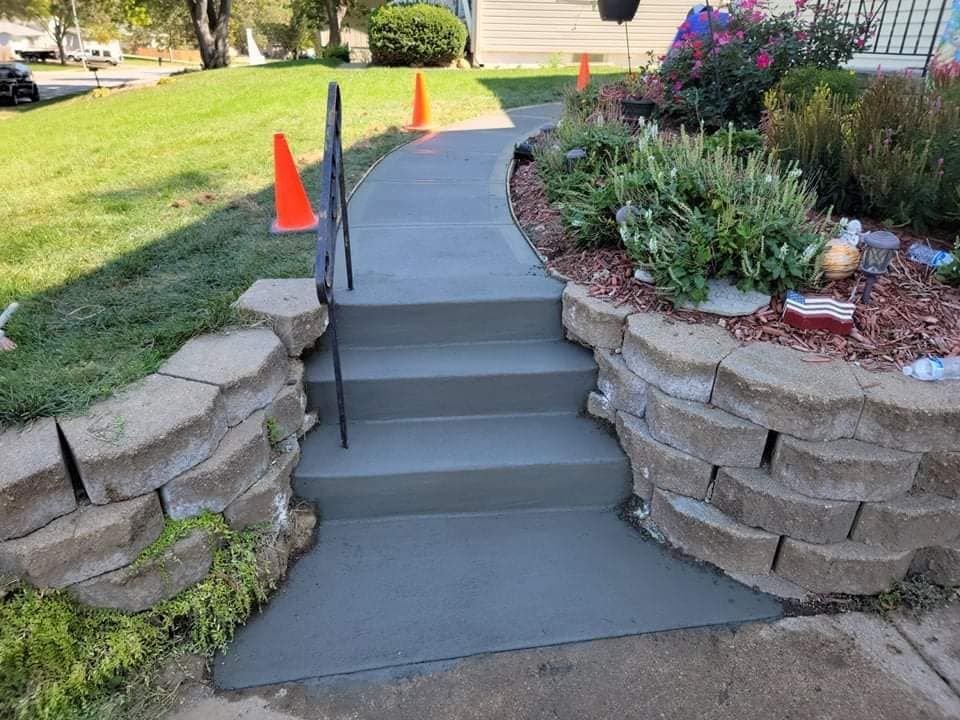A concrete walkway with stairs leading up to a stone wall