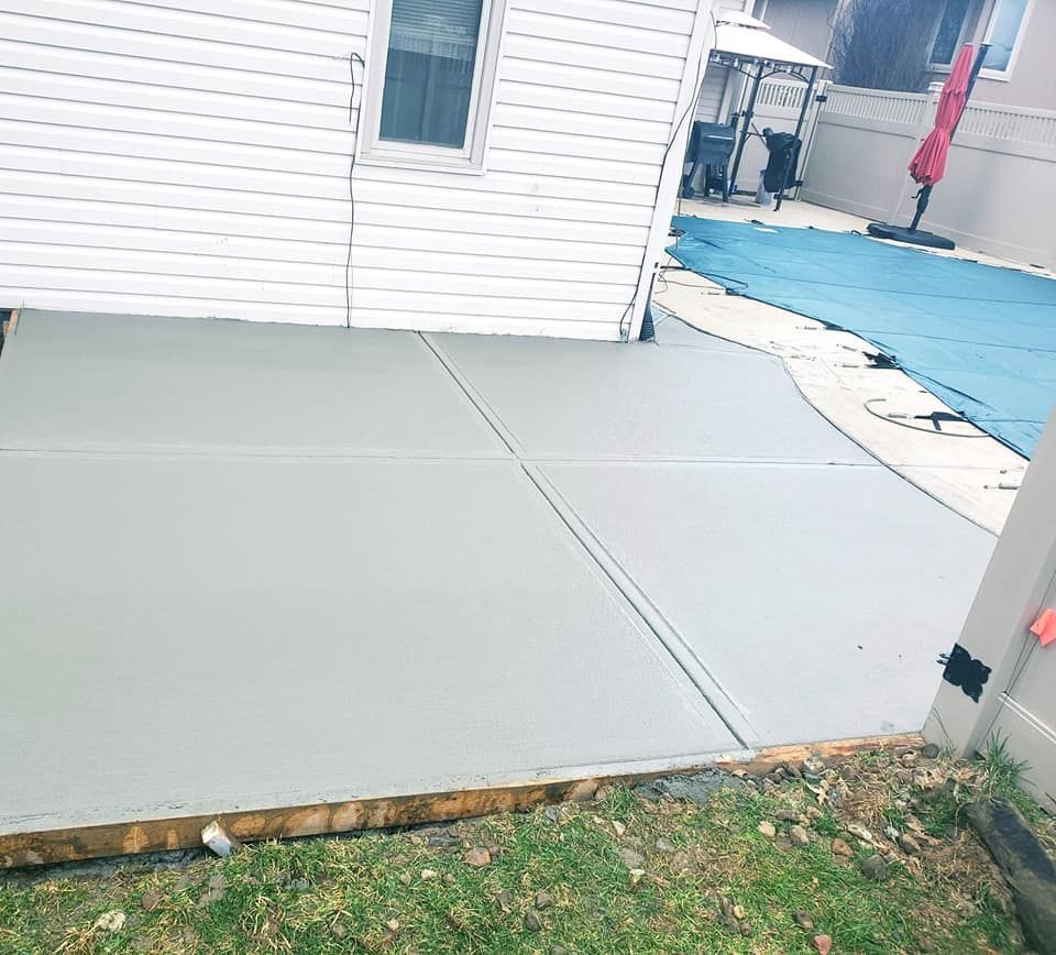 A concrete patio in front of a house next to a pool