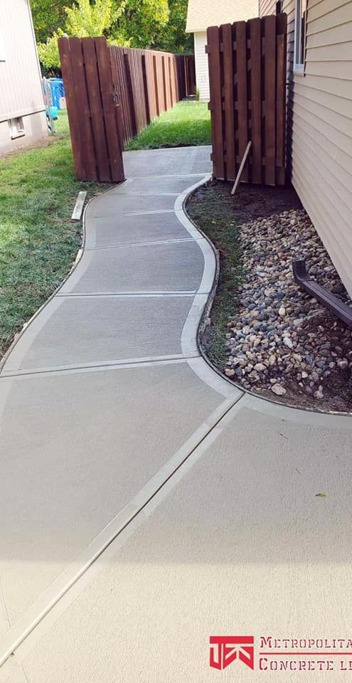 A concrete walkway leading to a house with a wooden fence