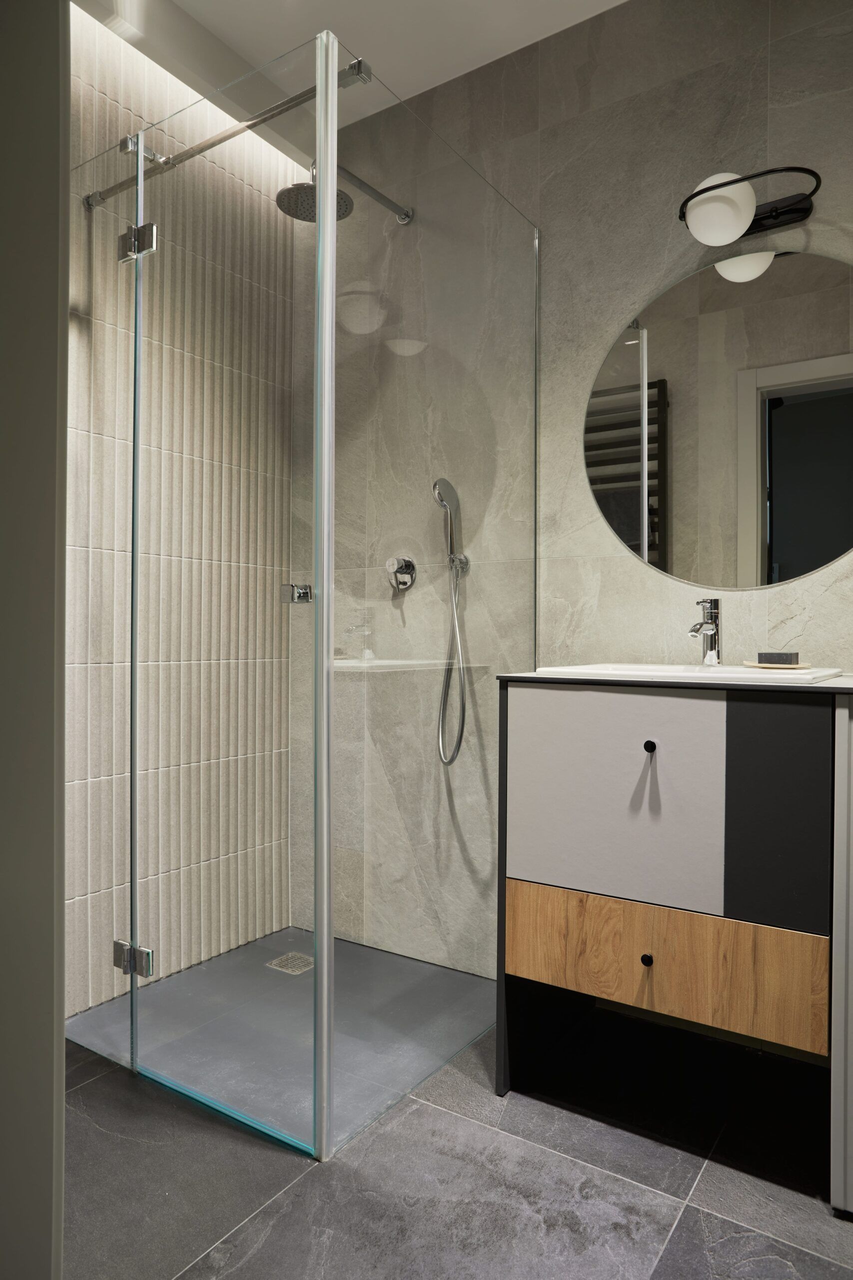 Modern bathroom with glass shower, gray walls, vanity, and round mirror.