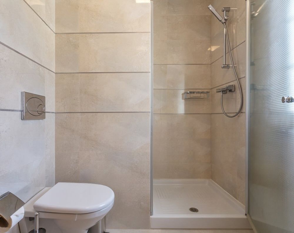 Bathroom with toilet and shower stall; cream-colored horizontal tile walls, frosted glass shower door.
