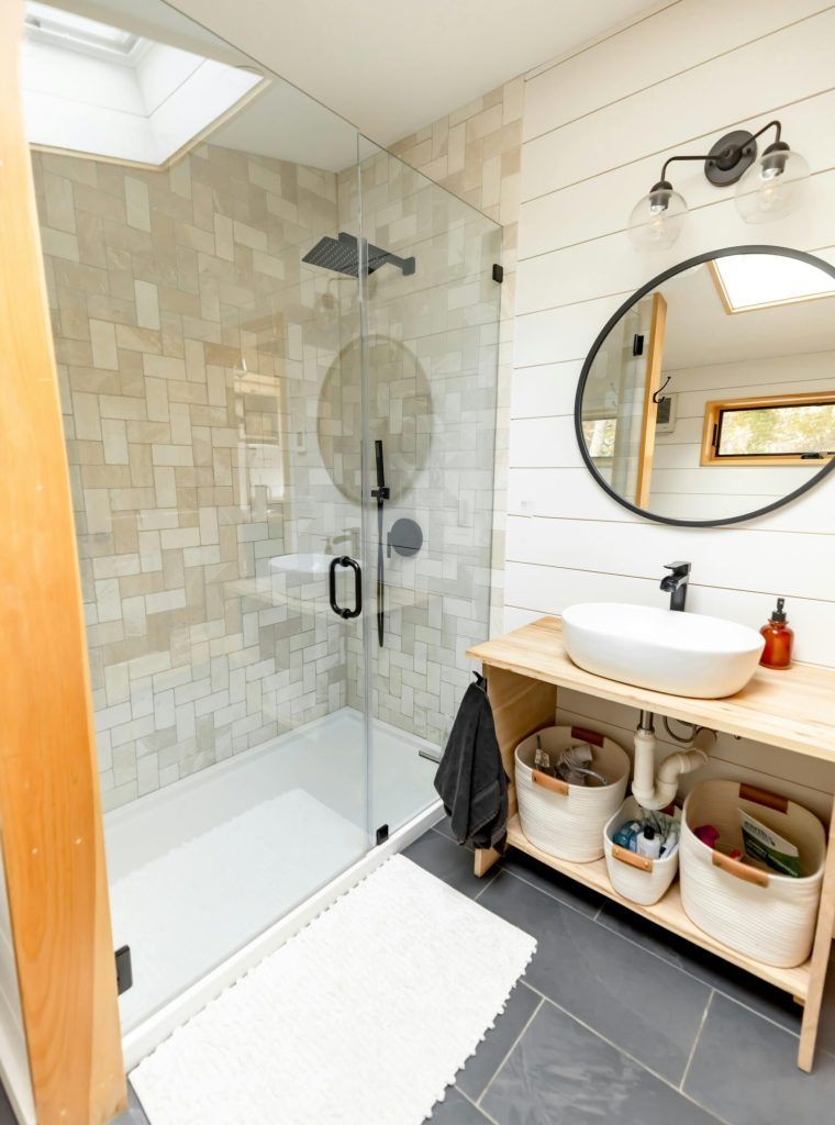 Bathroom with a shower, vanity, and round mirror. White shiplap walls, beige tile in shower.