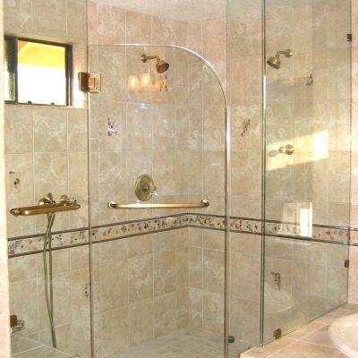 Glass shower enclosure with gold fixtures and beige tile.