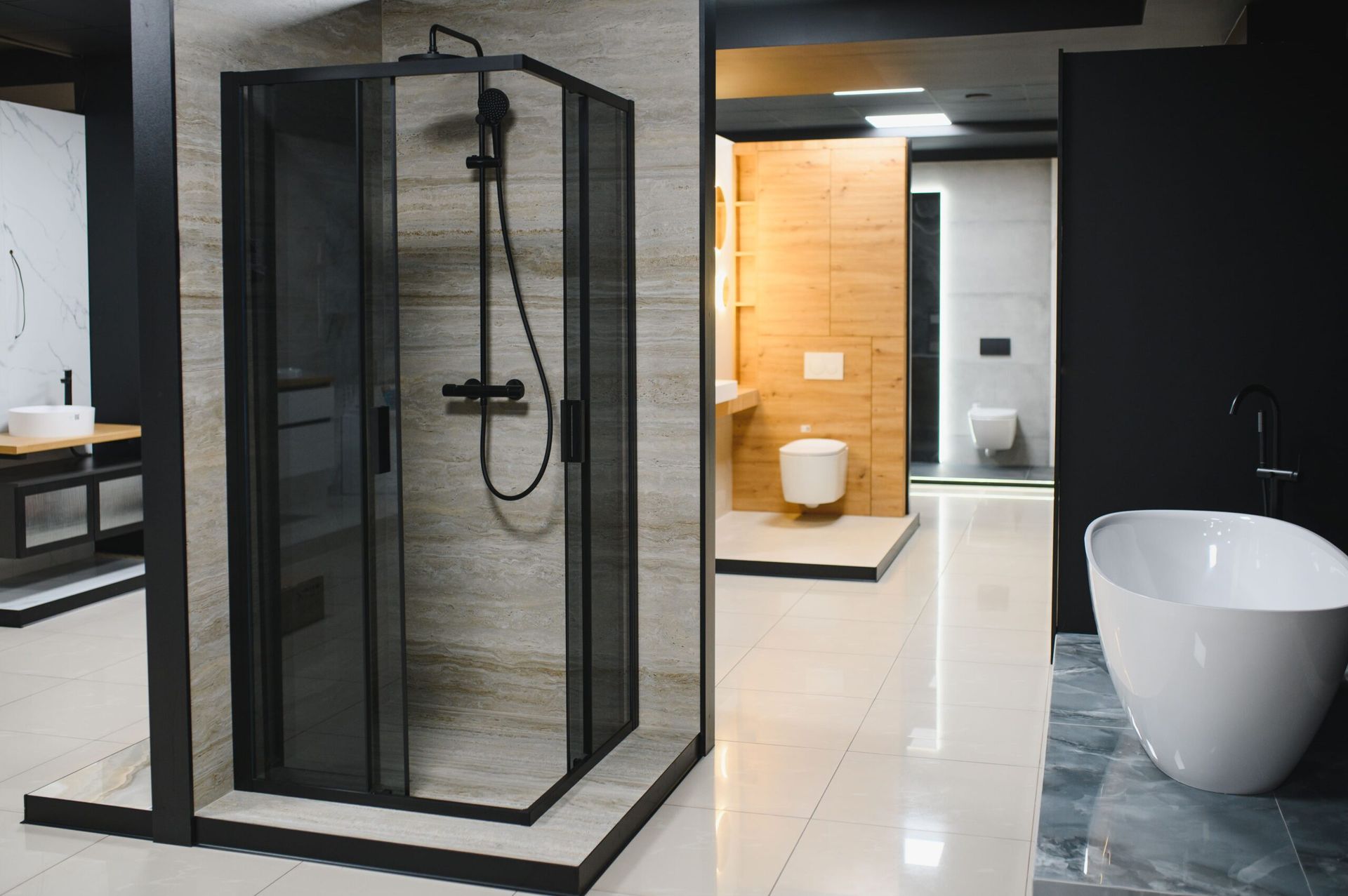 Black framed corner shower in a modern bathroom showroom with a white tub.