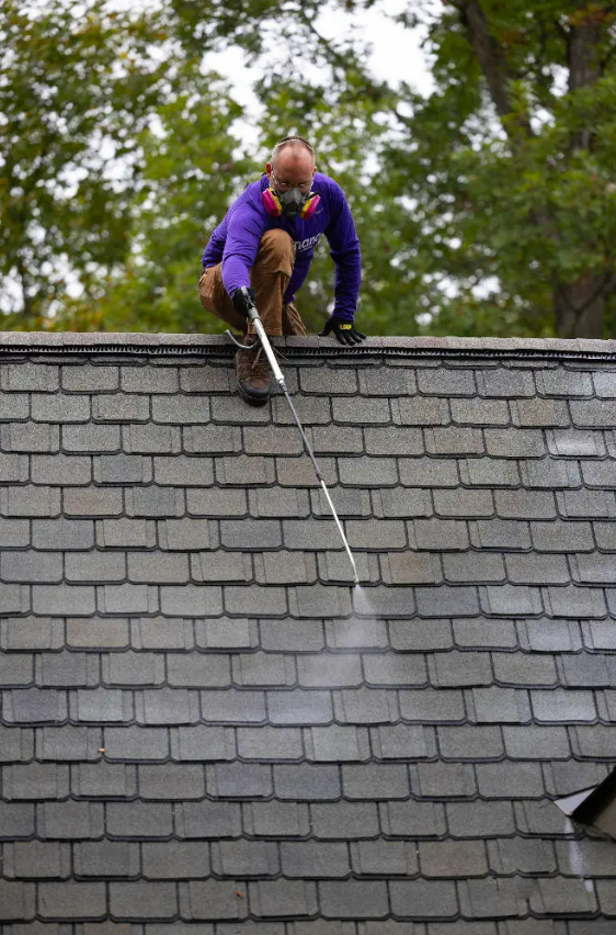 A man is cleaning a roof with a high-pressure washer.