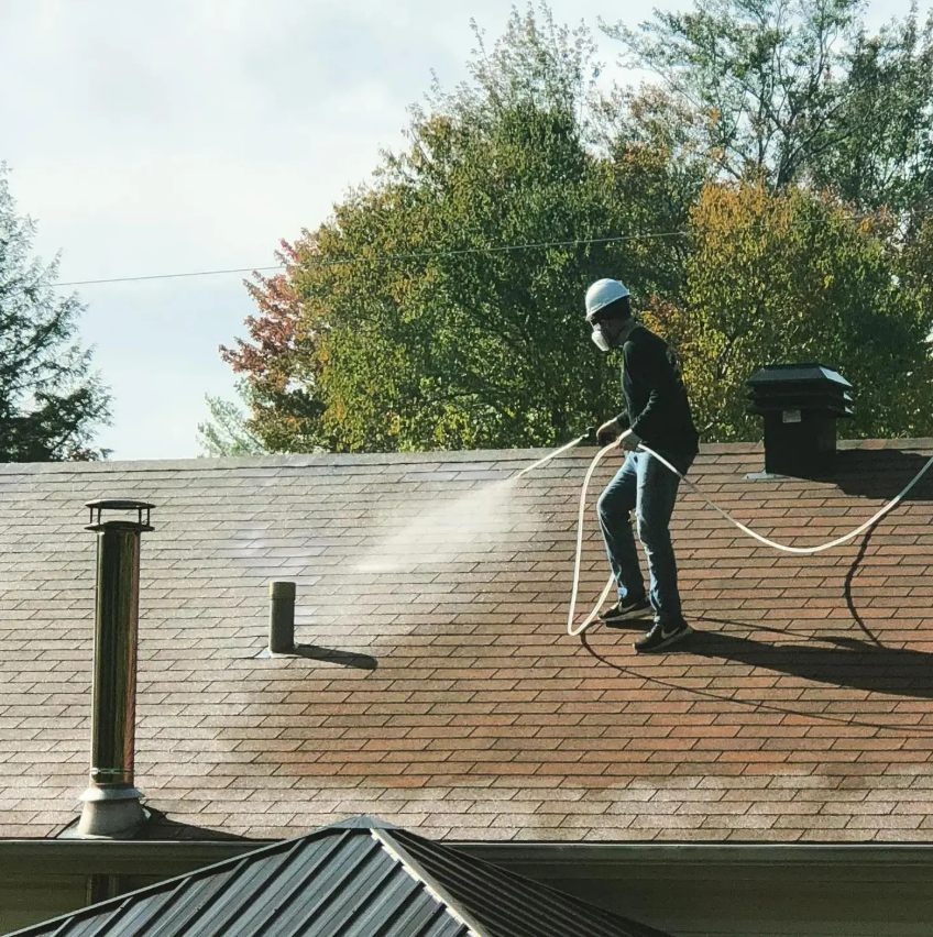 A man is spraying a roof with a hose.