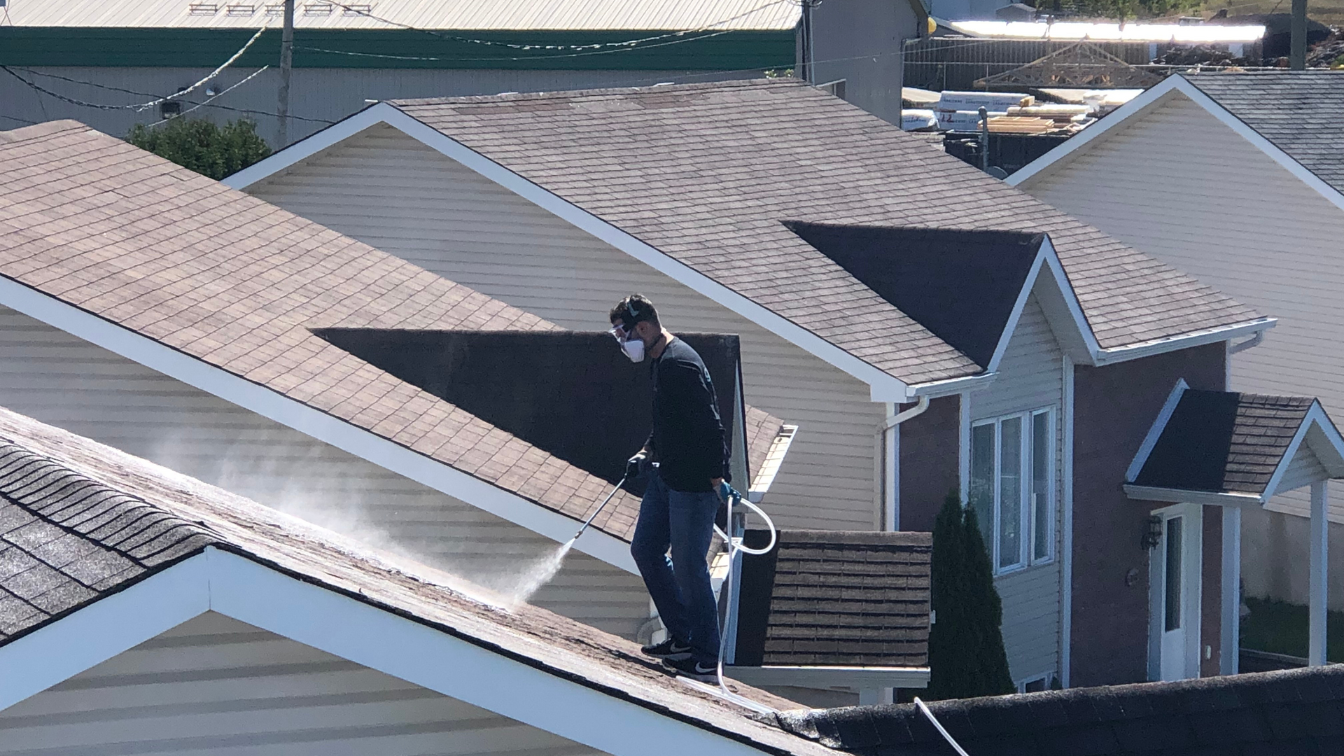 A man is cleaning the roof of a house with a high-pressure washer.