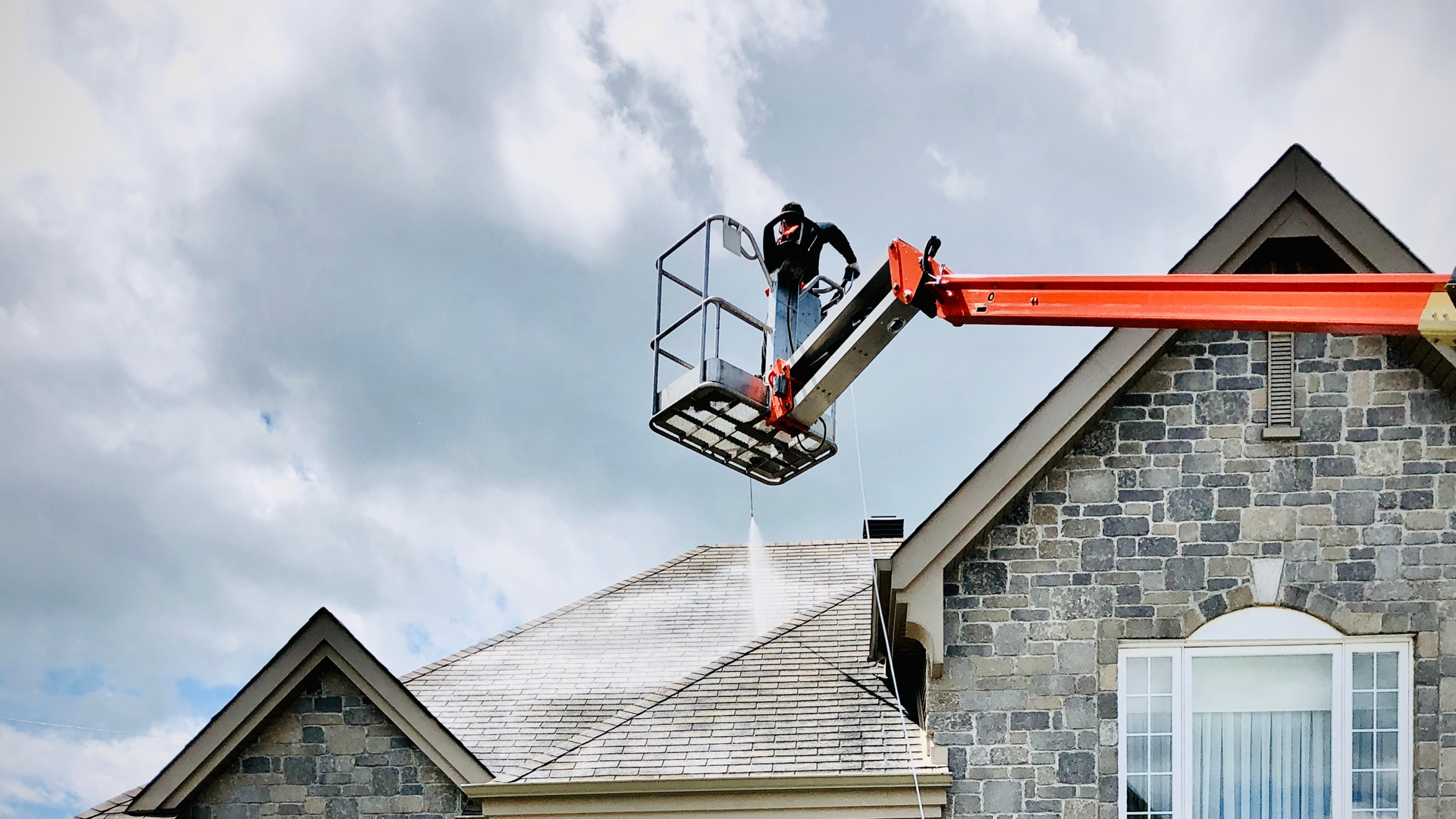 A man is cleaning the roof of a house with a crane.