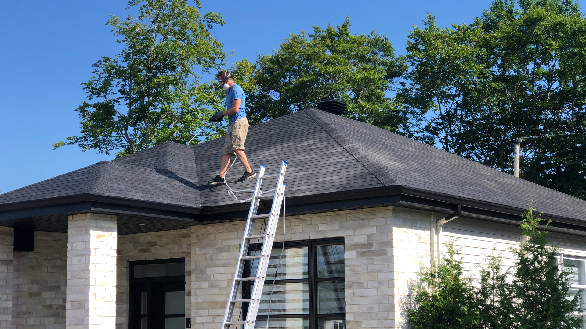 A man is standing on top of a ladder on the roof of a house.